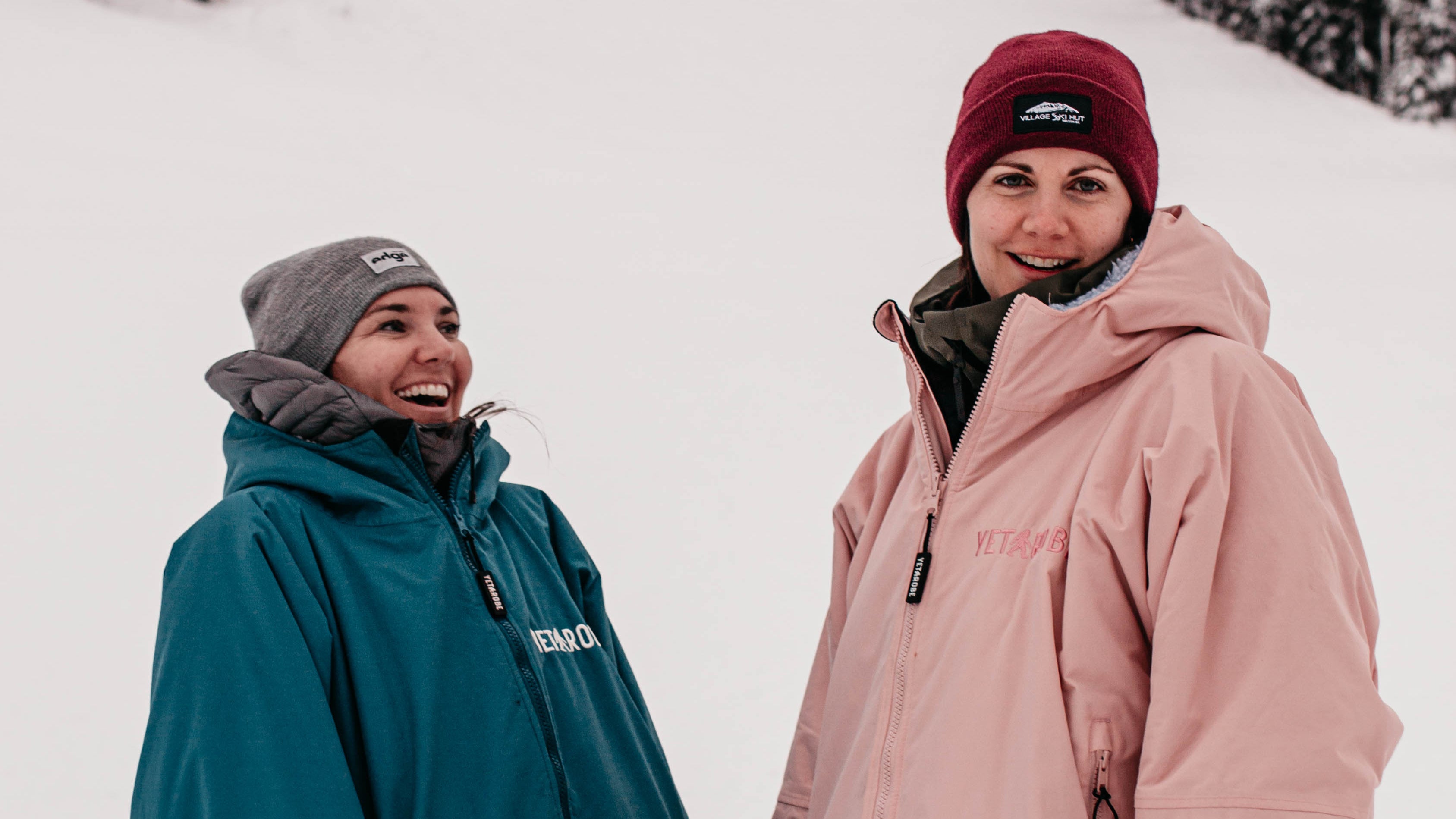 Two people in winter clothing standing in a snowy landscape with trees. YETIROBE