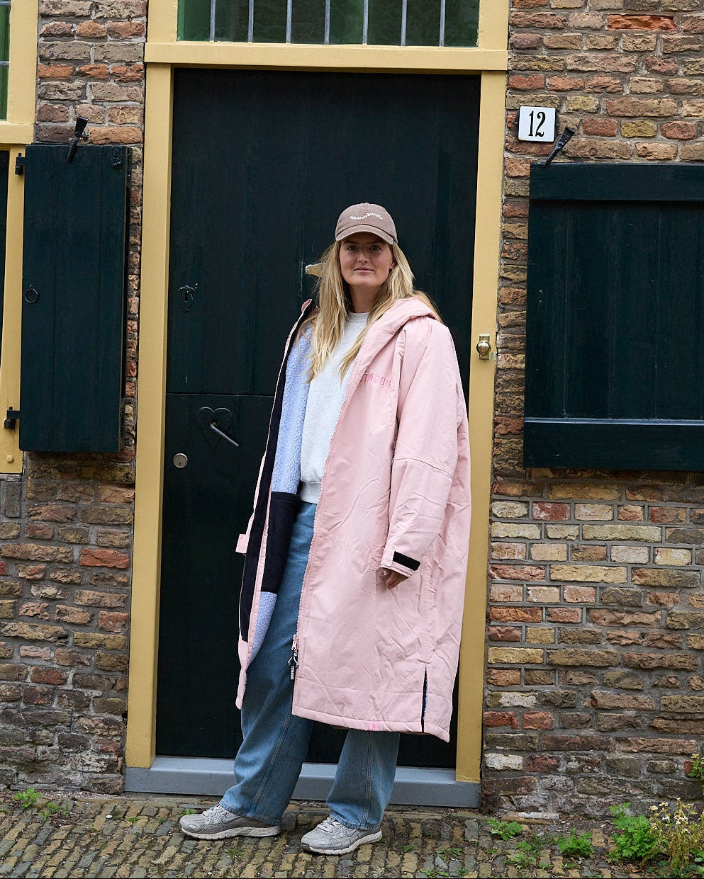 Woman in a pink coat standing in front of a brick building with a black door.