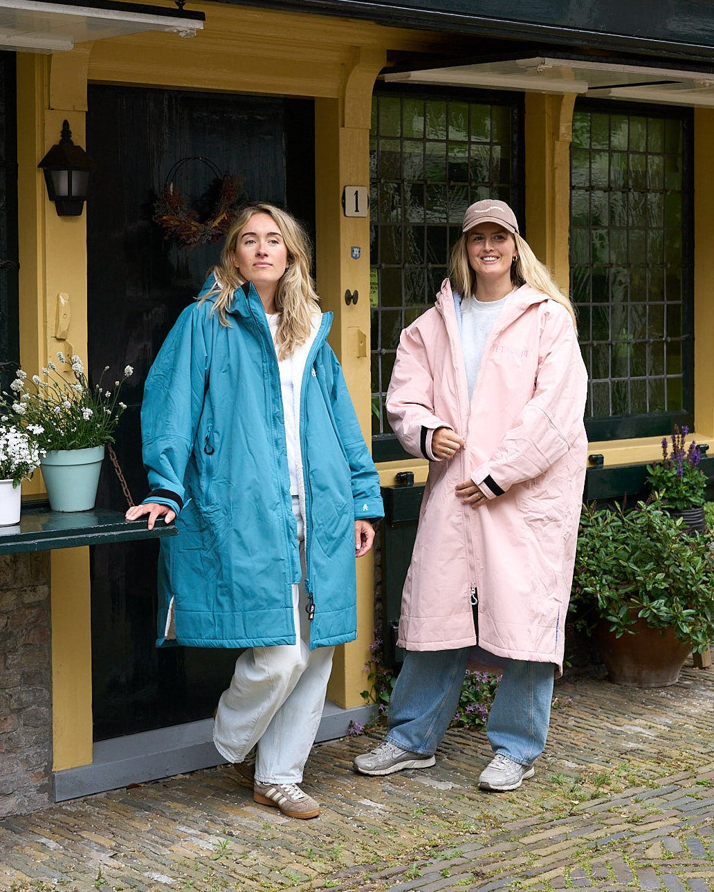 Two women standing outside a building, one in a blue coat and the other in a pink coat.