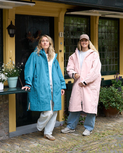 Two women standing outside a building, one in a blue coat and the other in a pink coat.